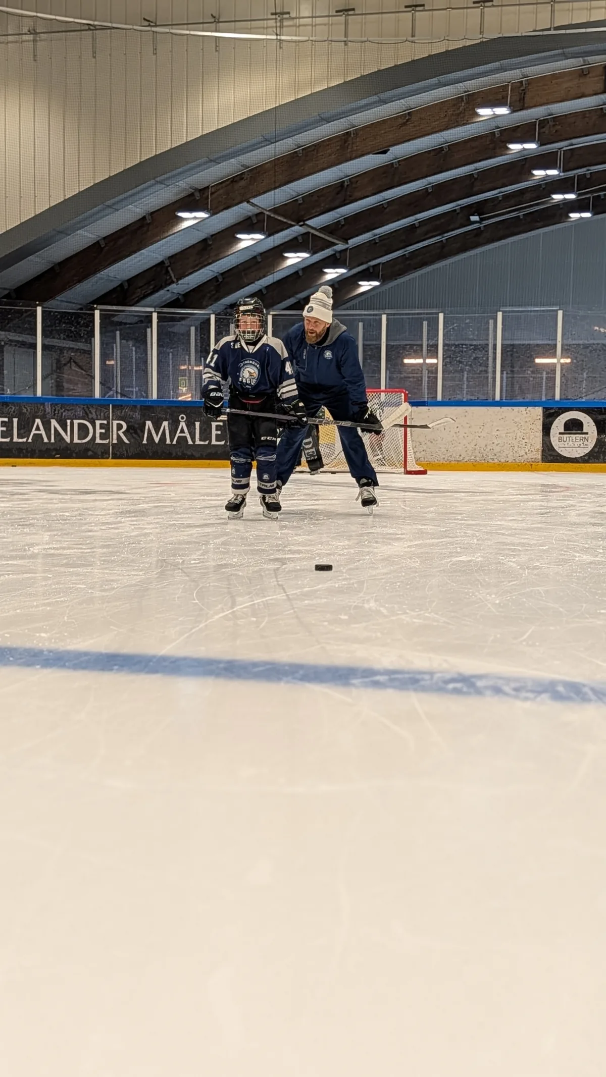 En tränare visar en Eagles-spelare en övning med klubba och puck på isen